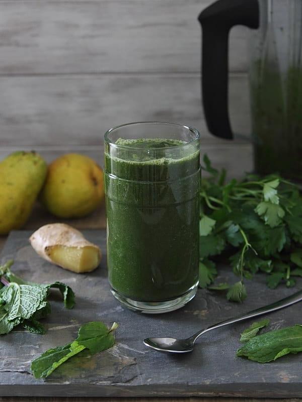 Αποτοξινωτικό Πράσινο Smoothie σε ποτήρι δίπλα σε ένα κουτάλι και πράσινα λαχανικά.