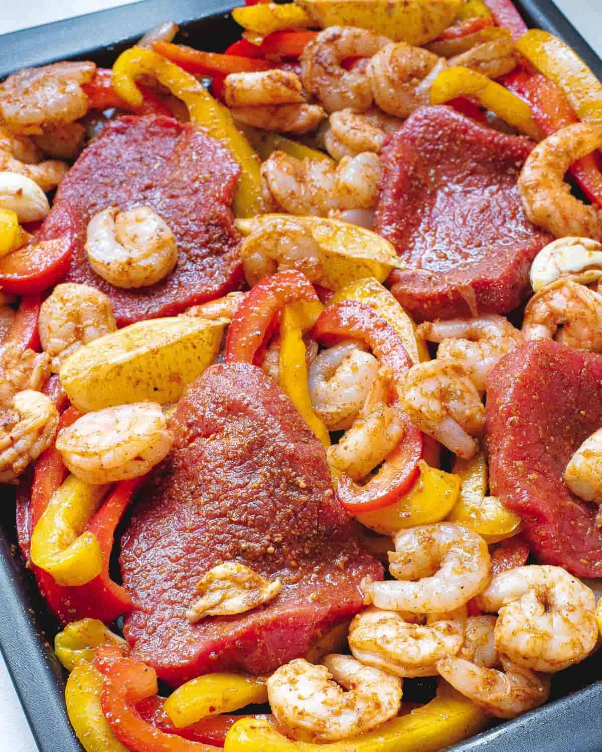 Sirloin steak, shrimp, peppers and onions tossed in fajita seasoning on a baking sheet. Sirloin steak, shrimp, peppers and onions tossed in fajita seasoning on a baking sheet.