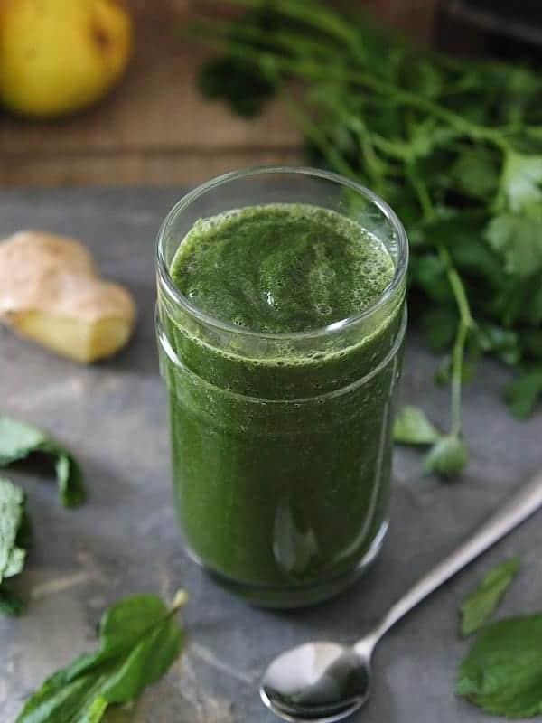 Πράσινο αποτοξινωτικό smoothie σε ποτήρι δίπλα σε ένα κουτάλι.
