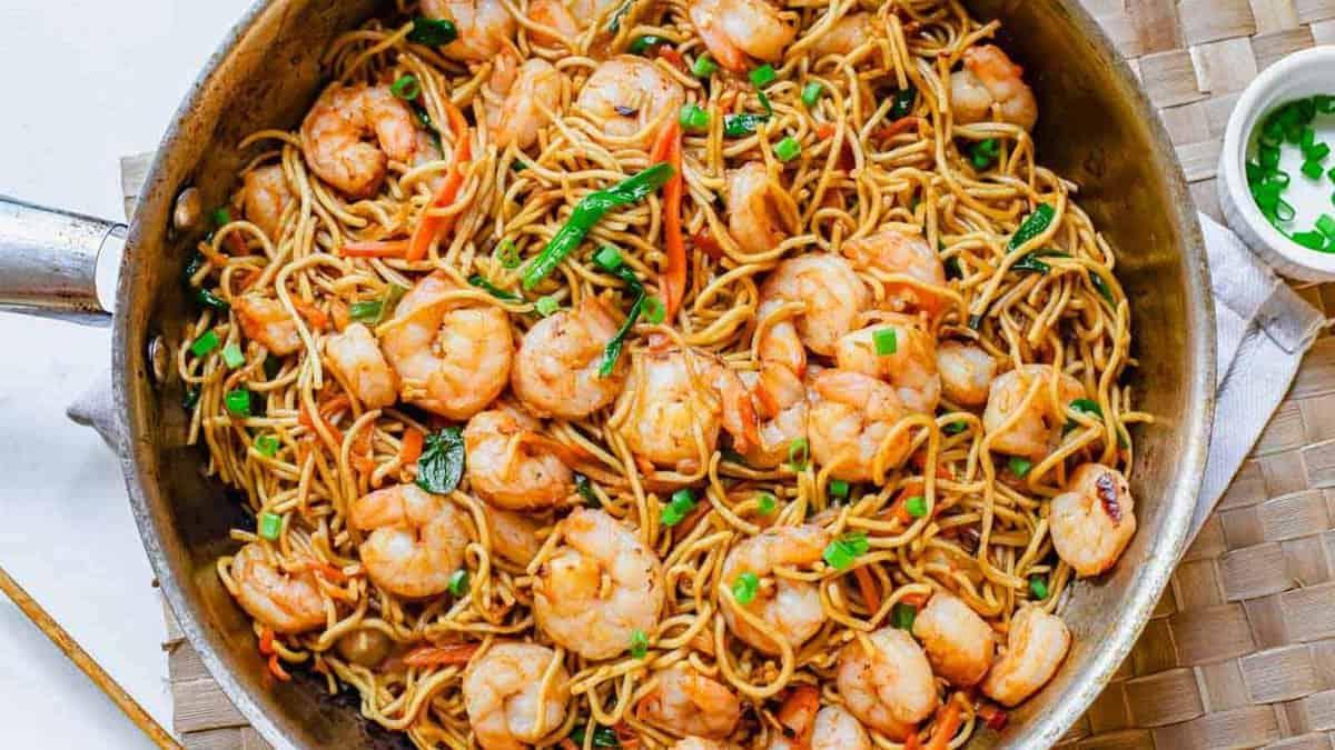 **Wok: 23 Ασιατικά Πιάτα που θα ξεπεράσουν το Takeout** 4 Γαρίδες lo mein σε ένα τηγάνι με ψιλοκομμένο φρέσκο κρεμμύδι σε ένα λευκό μπολ στο πλάι.