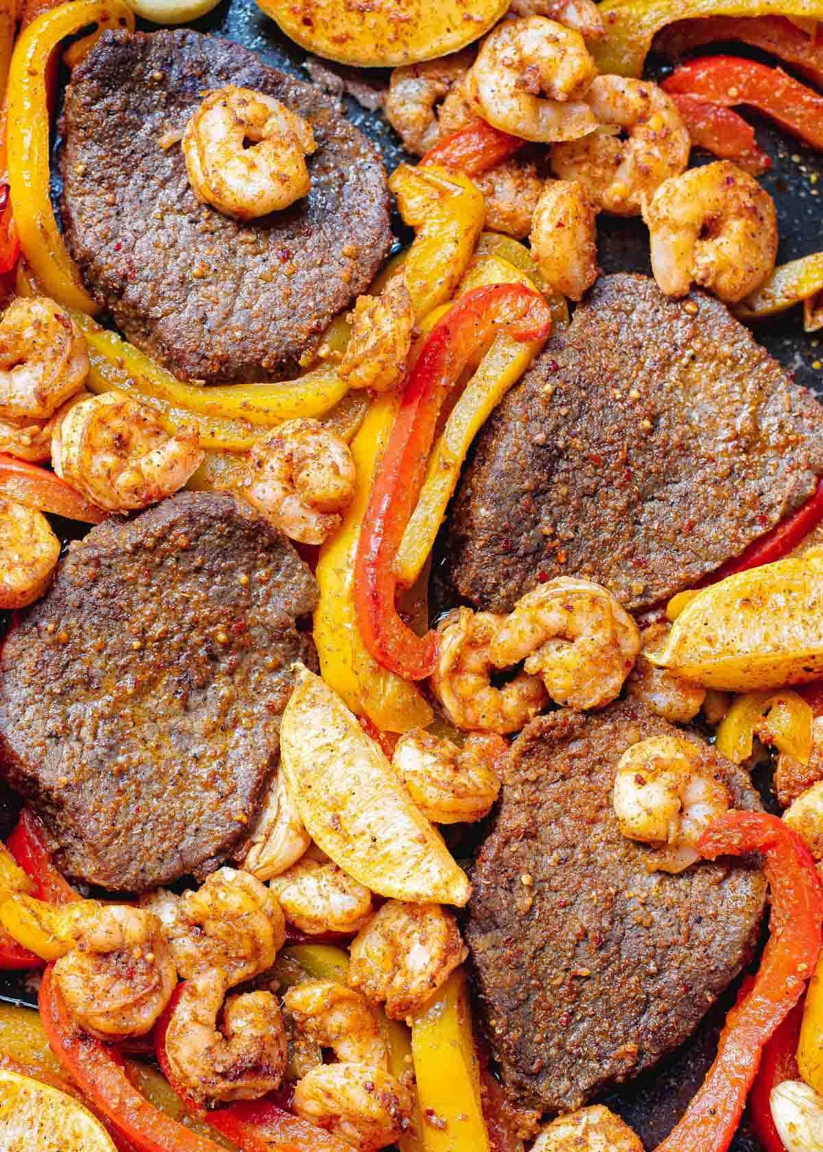 Cooked steak, shrimp, peppers and onions on a sheet pan. Cooked steak, shrimp, peppers and onions on a sheet pan.