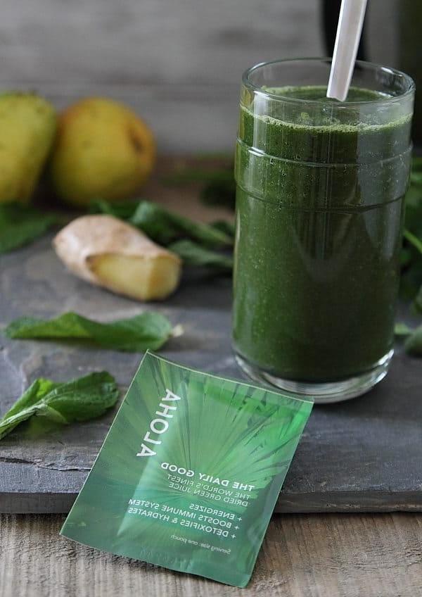 Πράσινο αποτοξινωτικό smoothie σε ποτήρι με καλαμάκι δίπλα σε ένα πακέτο σκόνης superfood.