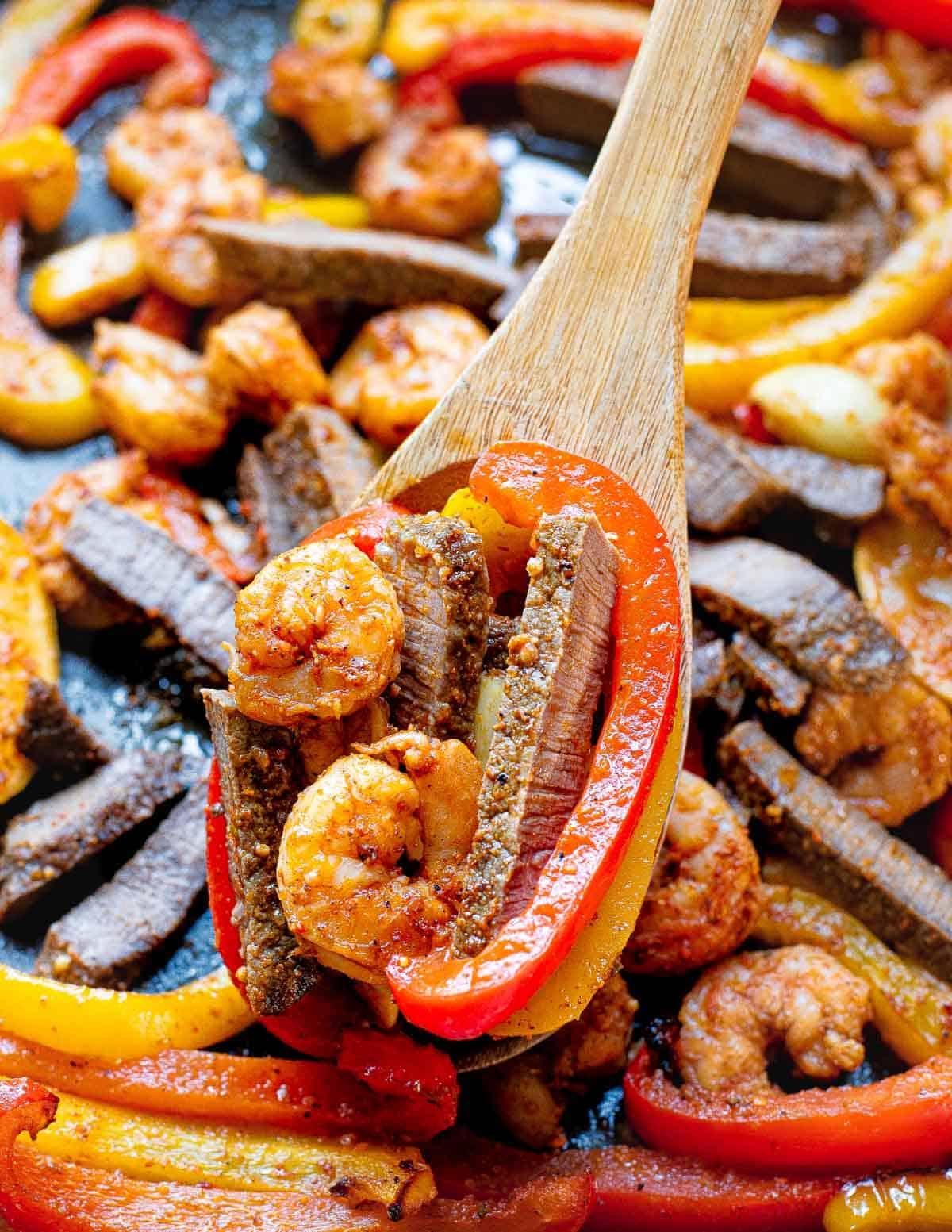 Shrimp and steak fajitas on a sheet pan with a wooden spoon. Shrimp and steak fajitas on a sheet pan with a wooden spoon.
