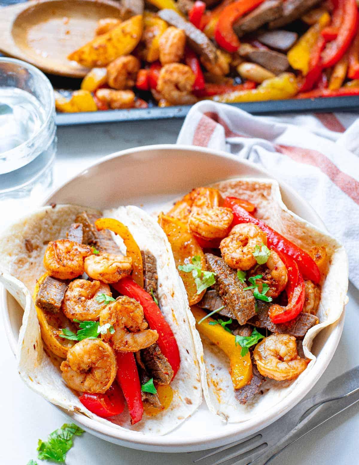 Steak and shrimp fajita recipe served in tortillas on a white plate. Steak and shrimp fajita recipe served in tortillas on a white plate.