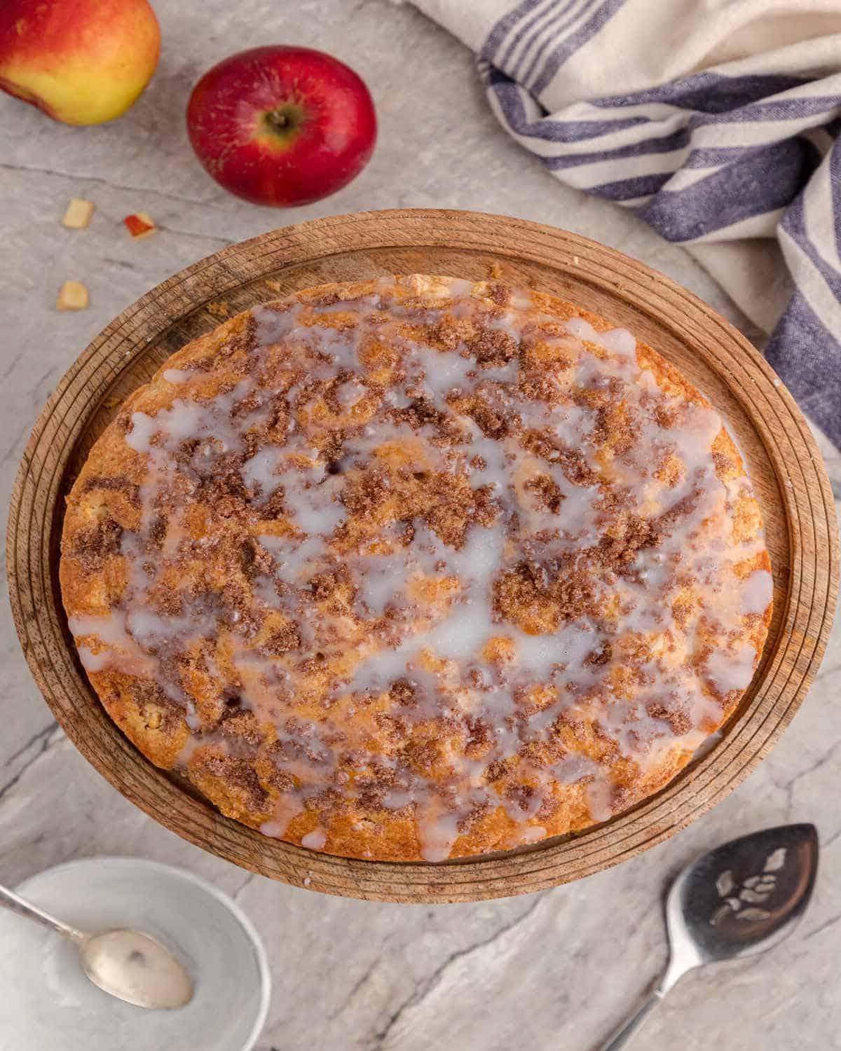 Μια φρεσκοψημένη μηλόπιτα crumble με επικάλυψη, συνοδευόμενη από ολόκληρα μήλα σε πάγκο κουζίνας.