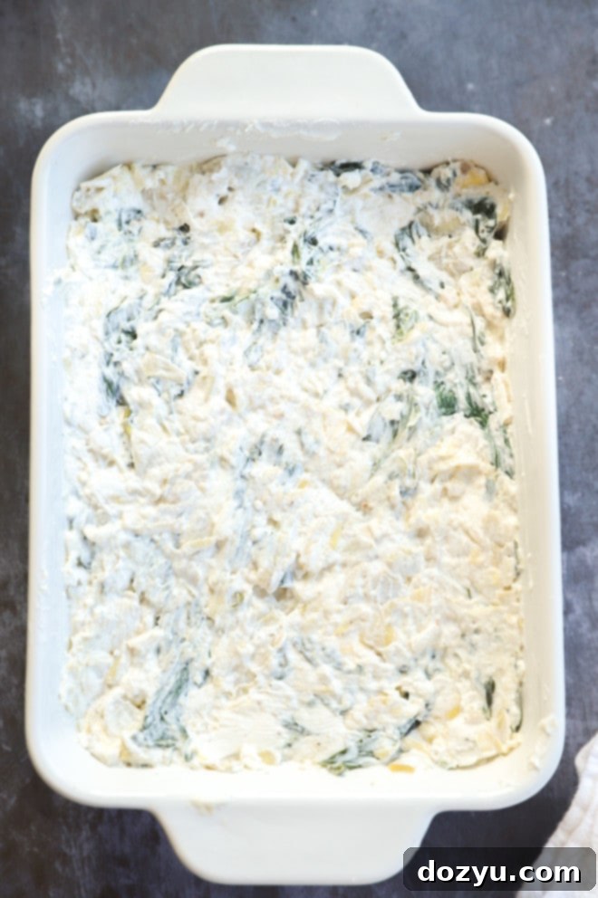 Creamy Spinach and Artichoke Goat Cheese Dip 6 Spinach and artichoke goat cheese dip before baking in a white casserole dish, topped with fresh mozzarella