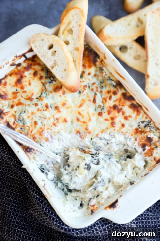 Creamy Spinach and Artichoke Goat Cheese Dip 8 Overhead view of a hot spinach and artichoke goat cheese dip in a white baking dish, surrounded by dippers