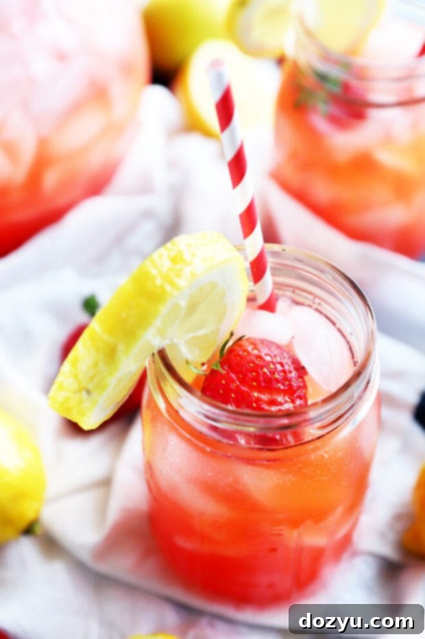 Refreshing Strawberry Vodka Lemonade 11 A mason jar filled with a vibrant berry-colored drink, garnished with fresh berries and mint, set on a wooden surface.