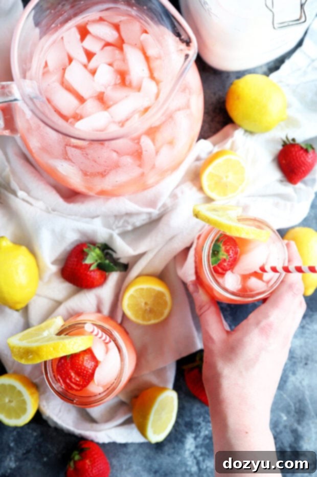 Refreshing Strawberry Vodka Lemonade 12 A hand holding a mason jar of vibrant pink vodka strawberry lemonade with a straw, against a bright outdoor background.