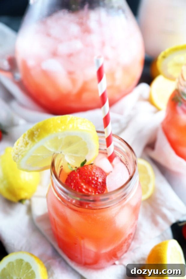 Refreshing Strawberry Vodka Lemonade 5 A single mason jar filled with vibrant pink vodka strawberry lemonade, garnished with a lemon slice and a whole strawberry.