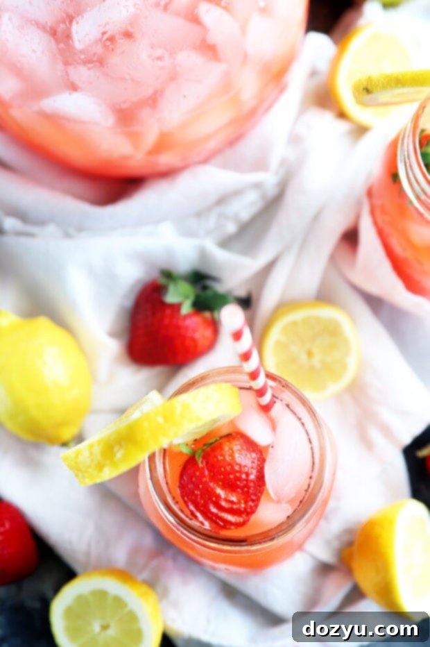 Refreshing Strawberry Vodka Lemonade 9 Overhead shot of a pitcher and two mason jars filled with vodka strawberry lemonade, surrounded by fresh lemons and strawberries.