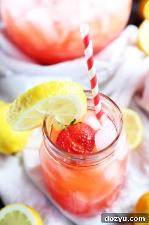 Refreshing Strawberry Vodka Lemonade 10 Close-up of a mason jar filled with pink vodka strawberry lemonade, with ice, and a lemon slice on the rim.
