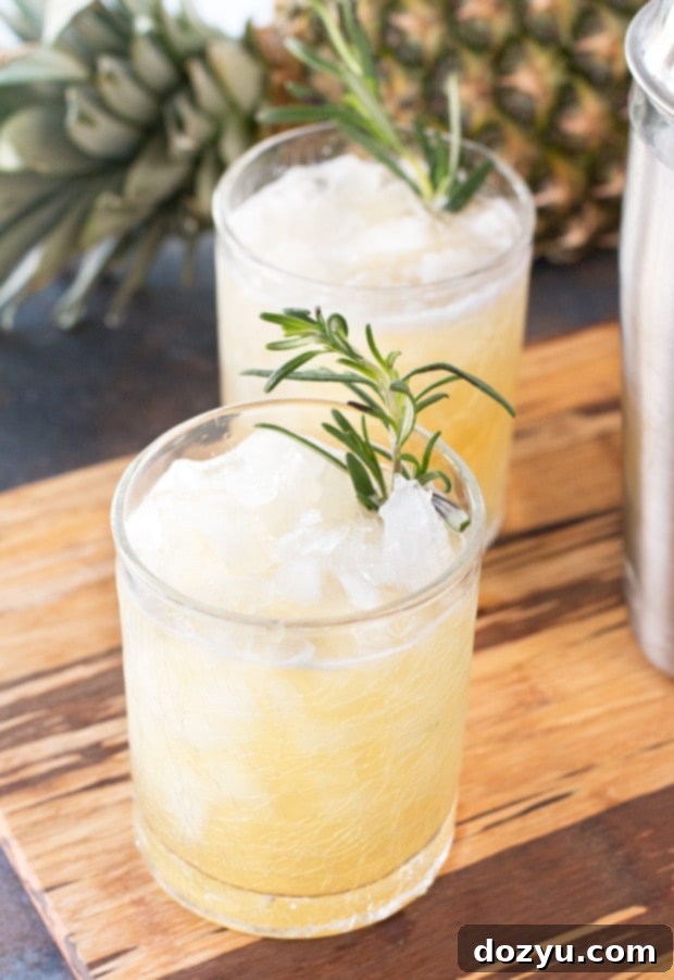The Pineapple Rosemary Smash 5 A perfectly prepared Pineapple Rosemary Smash cocktail, garnished beautifully with a sprig of rosemary and a wedge of fresh pineapple, glistening with ice.