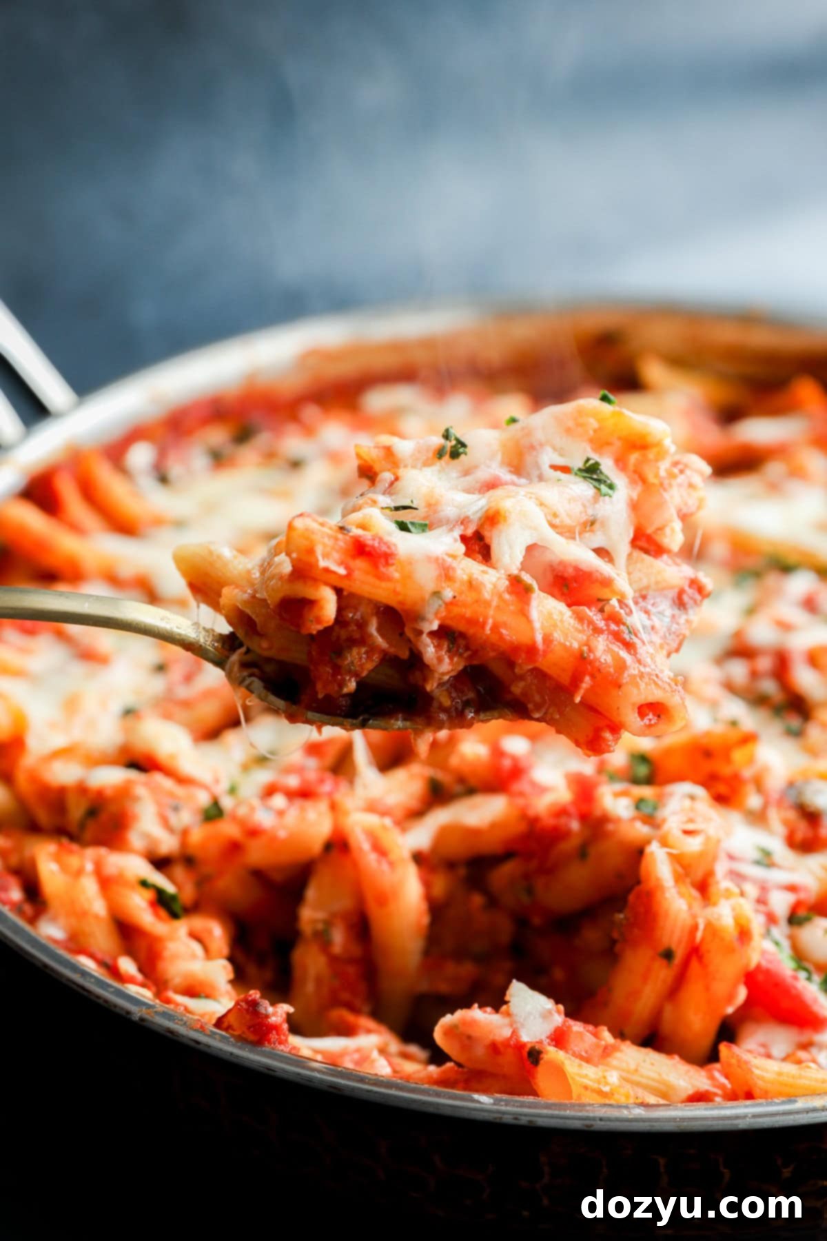 spoon lifting out italian penne dish with poultry and marinara sauce and cheese