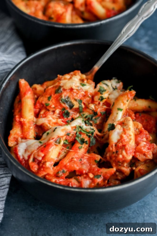a bowl of chicken parmesan pasta with a spoon and fresh basil on top