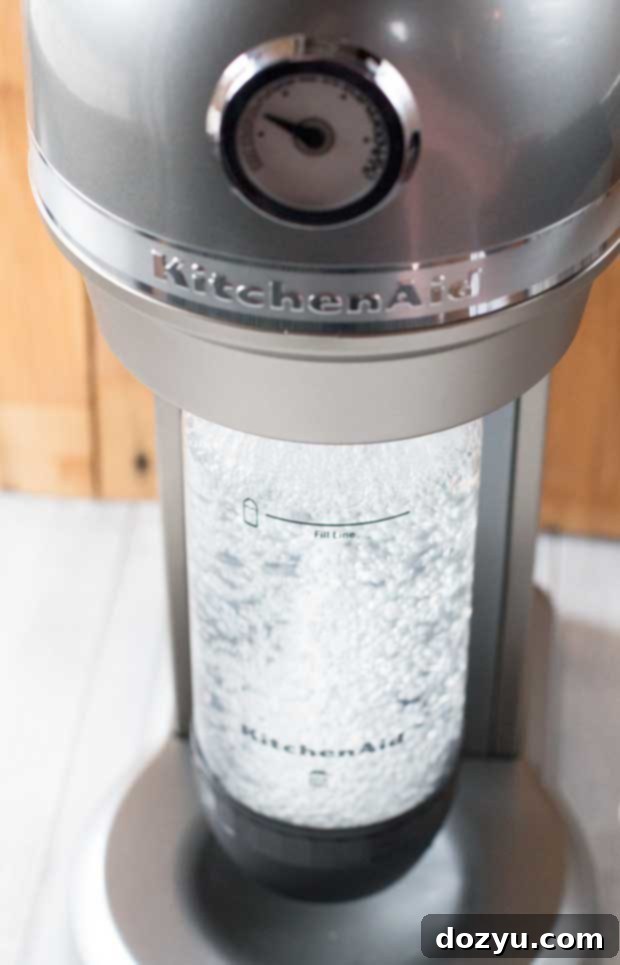 Close-up of a KitchenAid Sparkling Beverage Maker in action, creating fizzy drinks for homemade cocktails like Sparkling Bourbon Peach Lemonade