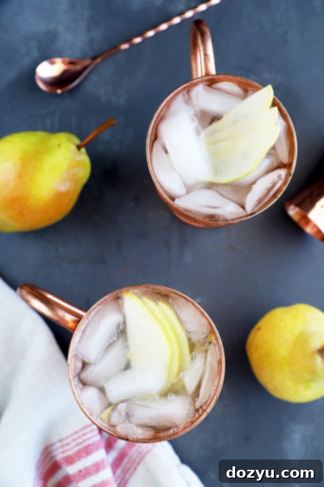 Pear Moscow Mule 2 Overhead view of two Pear Moscow Mules in elegant copper mugs, garnished with fresh pear slices and a sprig of thyme, on a rustic wooden table.