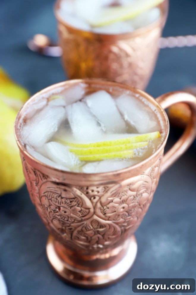 Pear Moscow Mule 3 Close-up of a single Pear Moscow Mule in a gleaming copper mug, adorned with a delicate fanned pear slice and a fresh herb, on a warm, inviting surface.