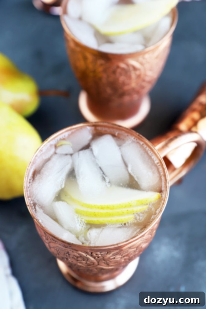 Pear Moscow Mule 4 Two chilled copper mugs filled with Pear Moscow Mules, beautifully garnished with fanned pear slices and a lemon twist, arranged on a rustic wooden board.