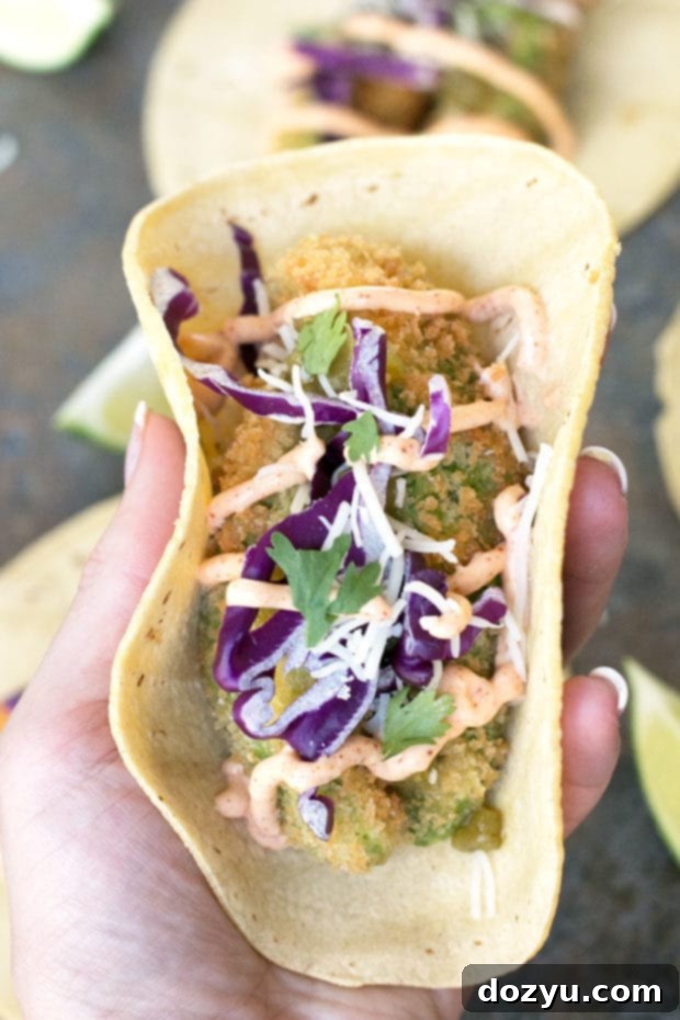 Close-up of a stack of golden-brown fried avocado tacos on a rustic wooden board