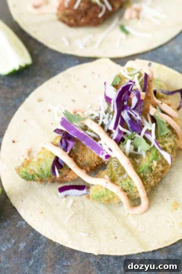 Beautifully arranged fried avocado tacos on a plate with fresh lime wedges and vibrant toppings