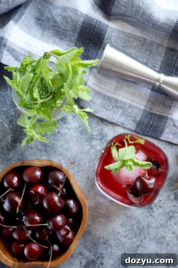 Cherry Bomb Whiskey Smash 4 Overhead view of a Cherry Whiskey Smash cocktail with fresh cherries, mint, and a lemon slice on a light background.