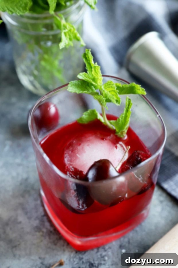 Cherry Bomb Whiskey Smash 6 Close-up shot of a Cherry Whiskey Smash cocktail in an old fashioned glass, garnished beautifully with fresh cherries and mint sprigs.