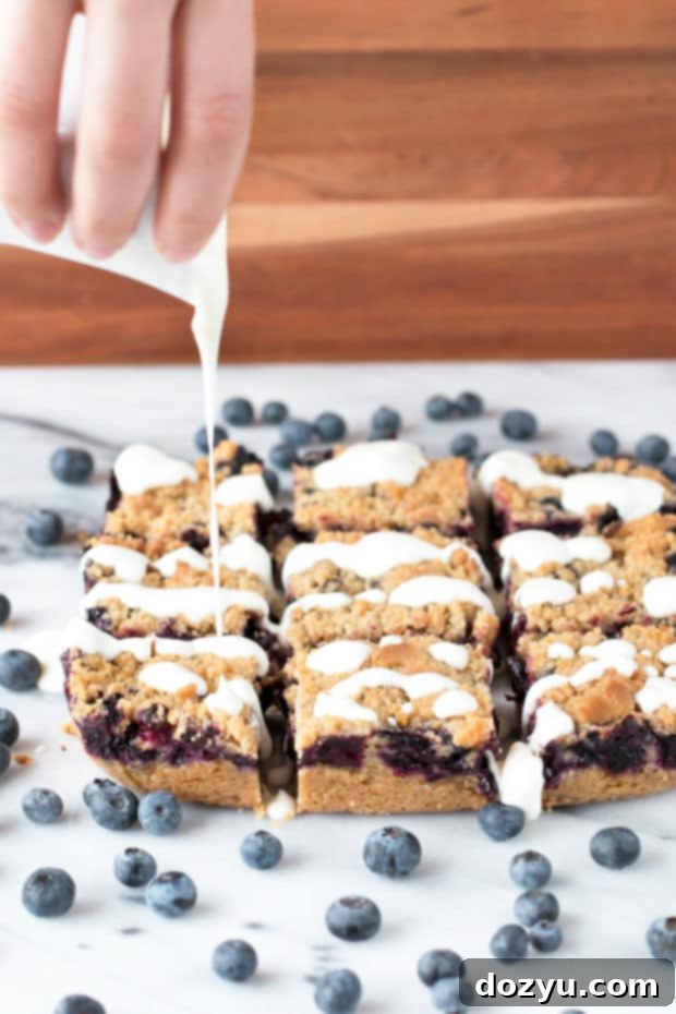 Blueberry Pie Crumb Bars arranged on a serving platter with a generous drizzle of cream cheese glaze