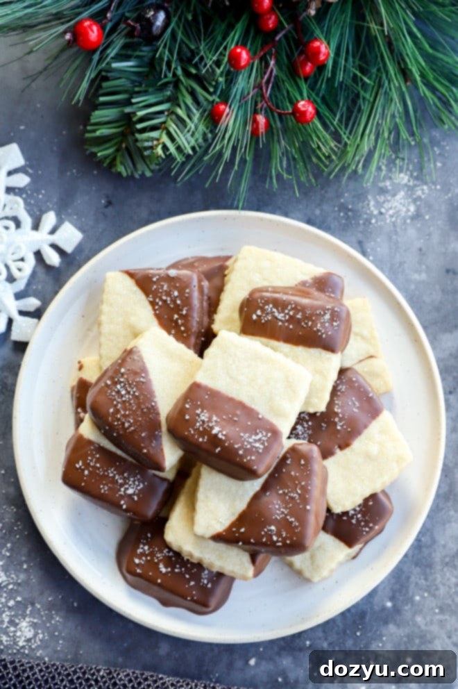 Decadent Milk Chocolate Dipped Shortbread 2 Plate of golden-baked shortbread cookies, half-dipped in luscious milk chocolate and sprinkled with flaky sea salt, arranged with festive holiday decorations.