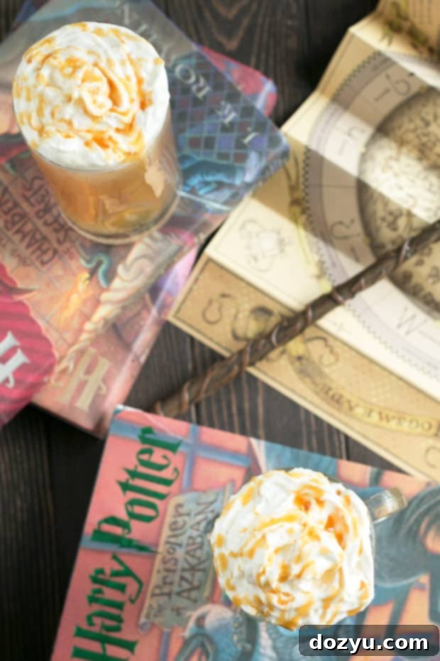 The author's hand holding a festive Butterbeer Cocktail, ready for a Harry Potter themed celebration. Highlighted are the creamy top and inviting amber color of the drink, set against a festive background.