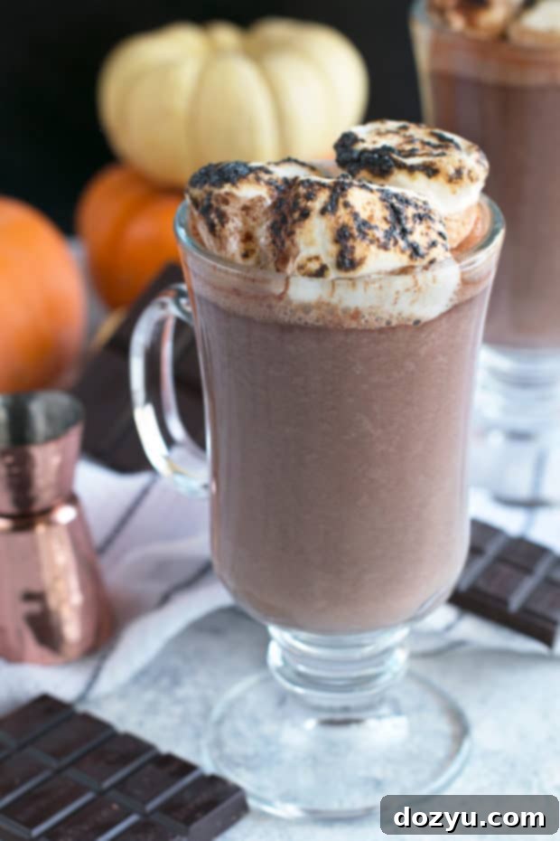 Close-up of creamy Pumpkin Bourbon Hot Chocolate with a spoon, highlighting the rich texture and inviting fall colors.