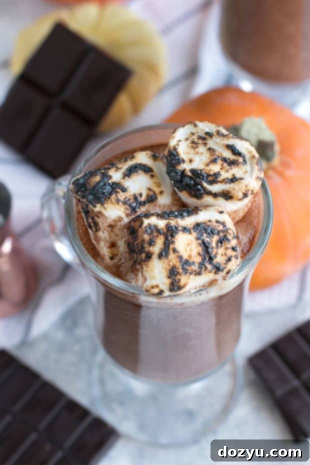 A mug of Pumpkin Bourbon Hot Chocolate, with a cozy sweater and autumnal decor in the background, perfect for a relaxing fall moment.