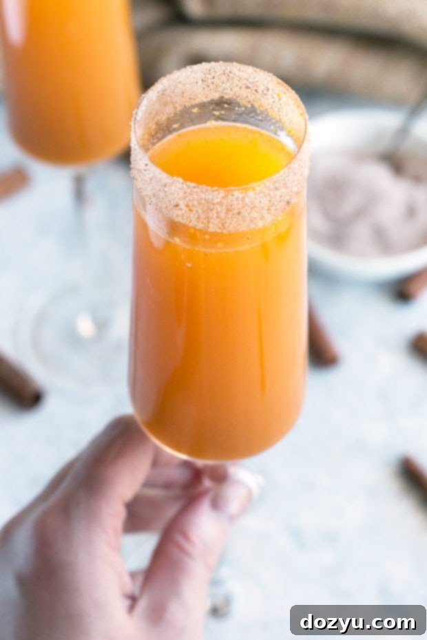 Spiced Pumpkin Mimosa 8 Two Pumpkin Pie Mimosas prepared in champagne flutes, garnished with whipped cream and cinnamon sticks, presented on a rustic wooden board.