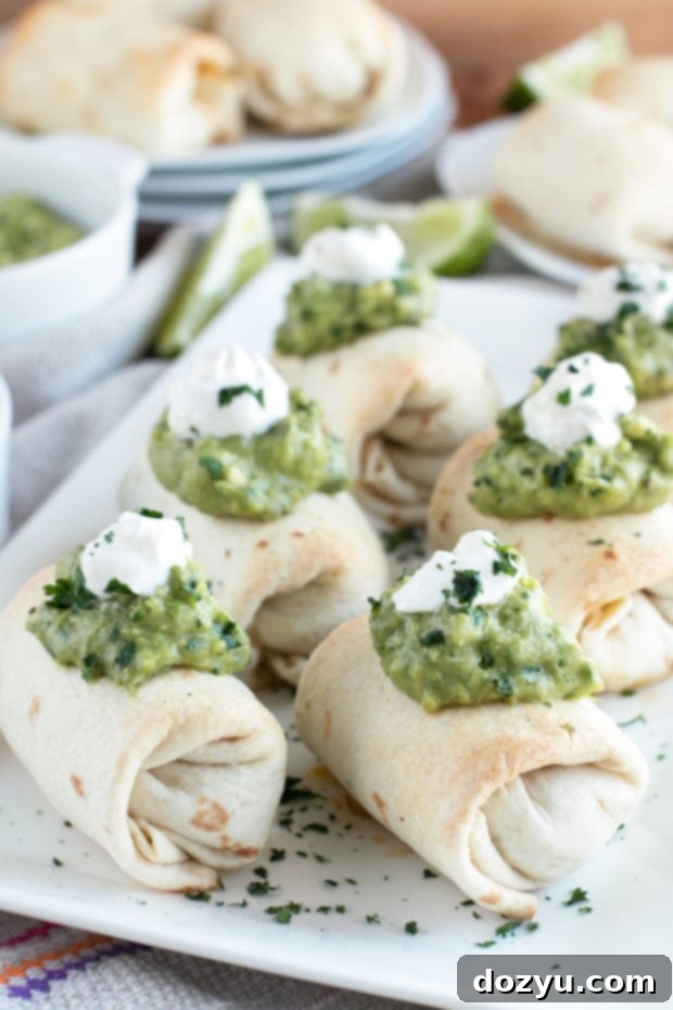 Golden Baked Chimichanga Bites with Spicy Avocado Dip 2 Golden brown baked mini chimichangas with creamy spicy guacamole on a wooden board.