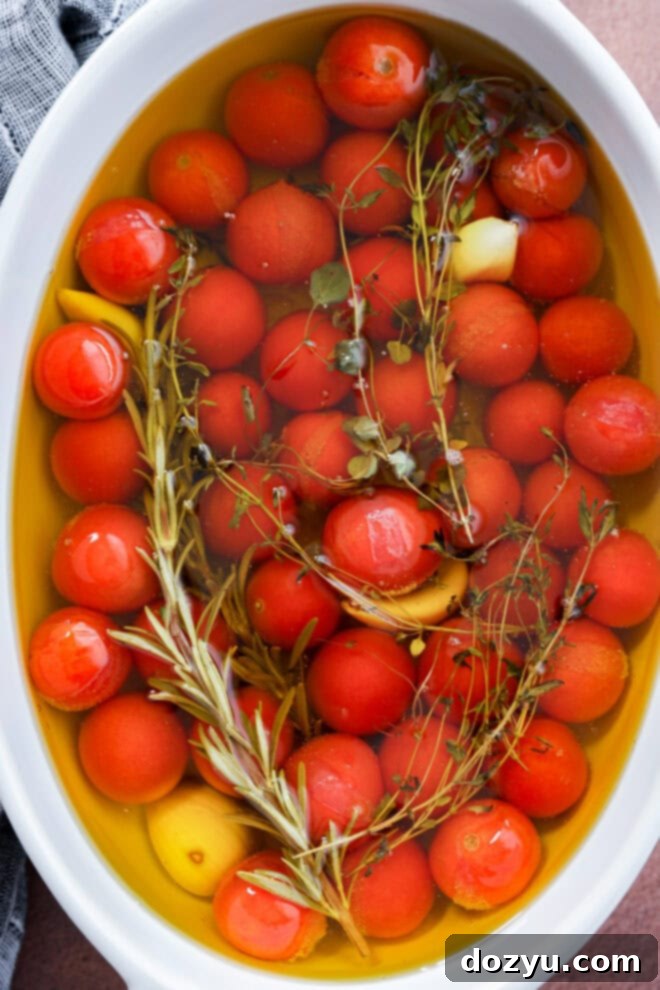 Easy Cherry Tomato Confit 5 Cherry tomato confit is made by submerging cherry tomatoes, garlic cloves, and fresh herbs like rosemary and thyme in olive oil in a white oval dish.