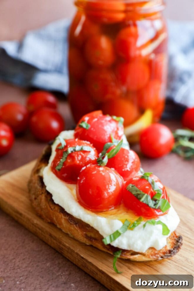 Easy Cherry Tomato Confit 7 A slice of toasted bread topped with creamy cheese, cherry tomatoes, and fresh basil sits on a wooden board. In the background, a jar filled with more cherry tomatoes is visible.