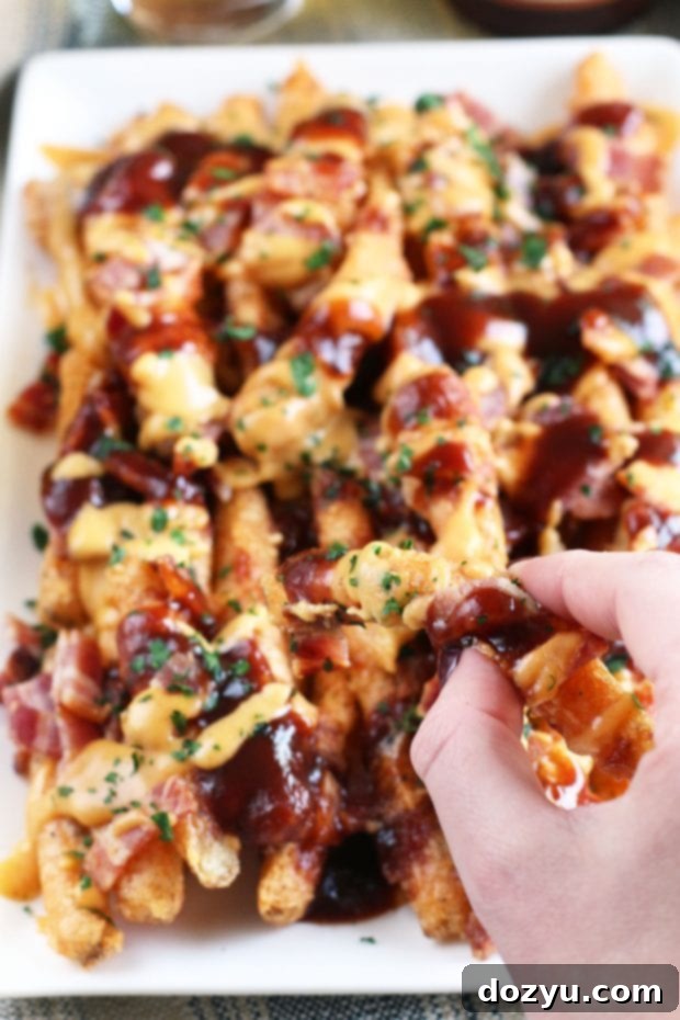Addictive BBQ Bacon Fries 6 A close-up of a single crispy beer-battered fry being dipped into the creamy spicy cheddar sauce