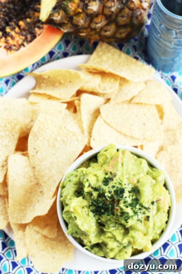 A bowl of Tropical Guacamole served in a molcajete, surrounded by fresh ingredients and tortilla chips