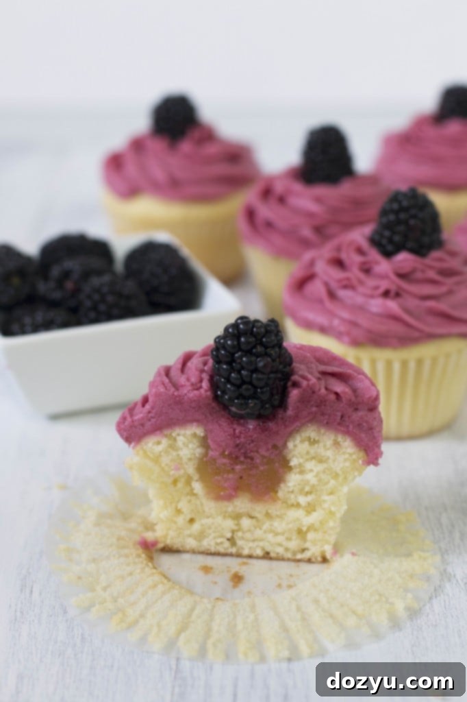 A vanilla cupcake cut in half, revealing a generous layer of zesty lemon curd filling inside