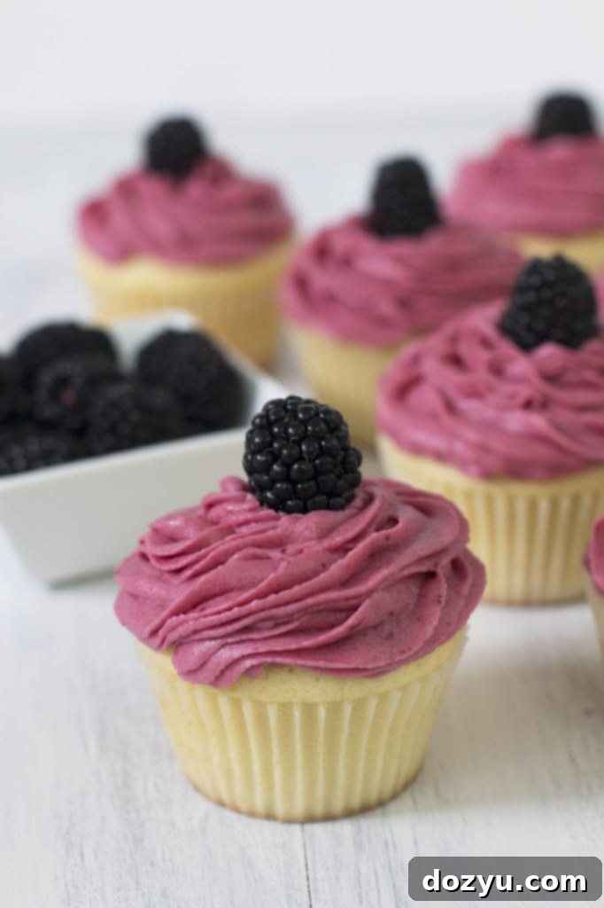 Close-up of perfectly frosted vanilla cupcakes adorned with fresh blackberries and a hint of lemon curd
