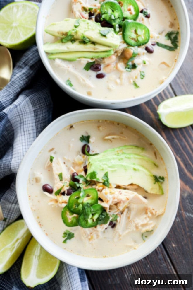 Velvety Slow Cooker White Chicken Chili 8 two bowls of soup with lots of toppings and lime wedges on the side