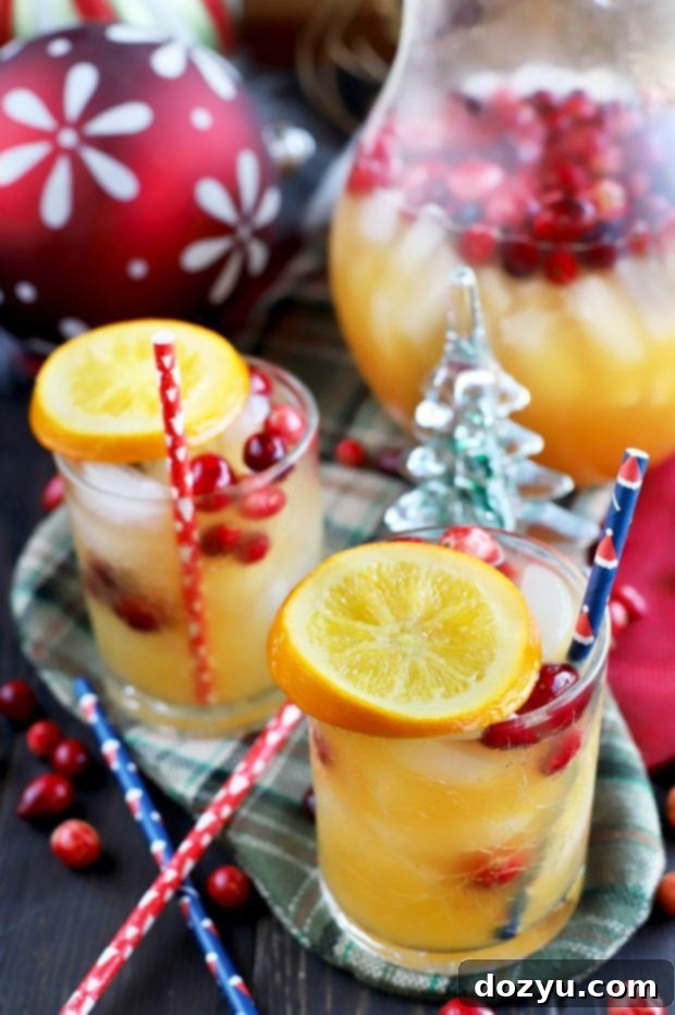 A large pitcher of Spiced Tropical Holiday Champagne Punch garnished with fresh cranberries and orange slices.