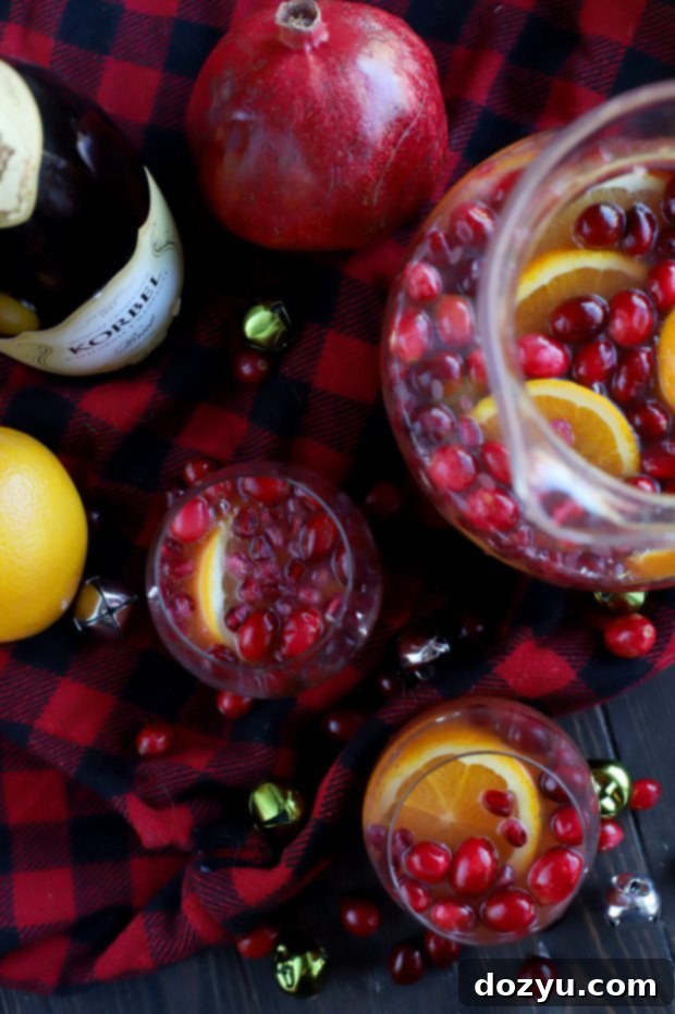 Vibrant Sparkling Holiday Brunch Punch in a large glass dispenser, garnished with fresh cranberries, orange slices, and pomegranate seeds.