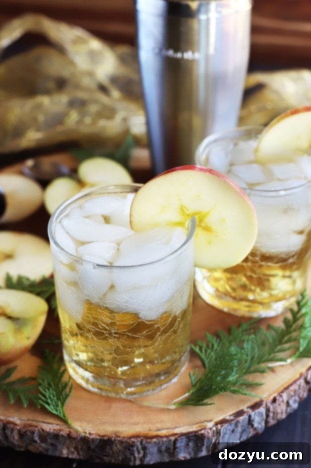 A tall glass of Smoky Mezcal Cider Cocktail with an apple slice garnish, set against a warm, inviting background.