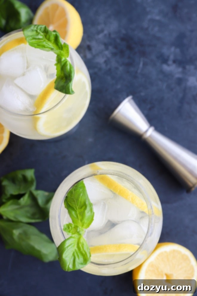Overhead image of lemon basil cooler cocktails in glasses, garnished with lemon wheels and fresh basil sprigs.