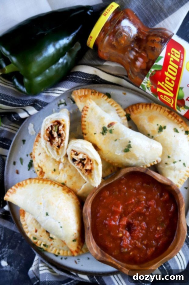 Poblano-Infused Chicken Enchilada Empanadas 2 A delicious pile of golden-brown Poblano Enchilada Chicken Empanadas, with one cut in half to show the rich filling, served alongside fresh LA VICTORIA® salsa for dipping.