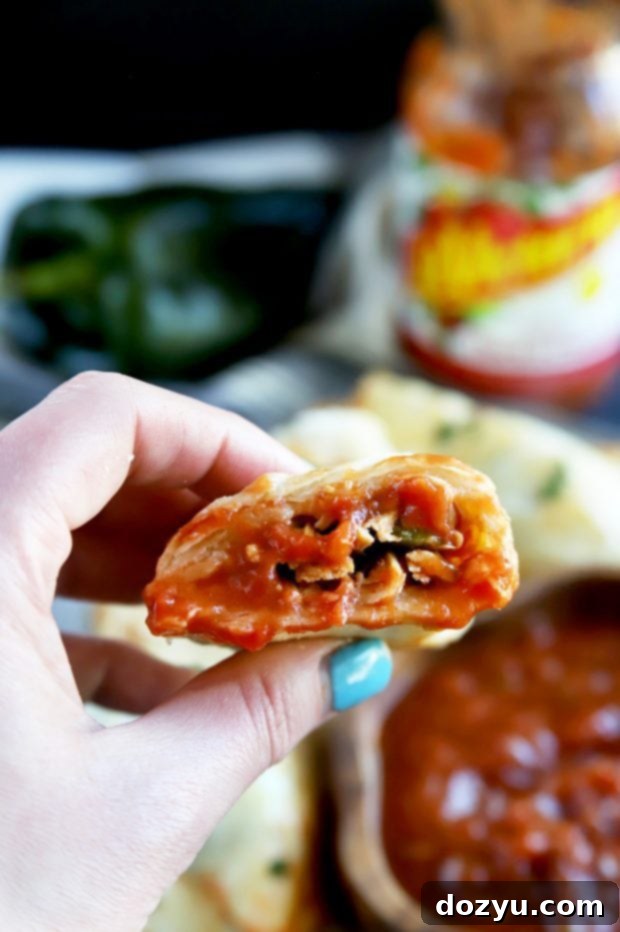 Poblano-Infused Chicken Enchilada Empanadas 11 A freshly baked Mexican hand pie, crispy and golden-brown, being dipped into a small bowl of rich red salsa, ready for a flavorful bite.