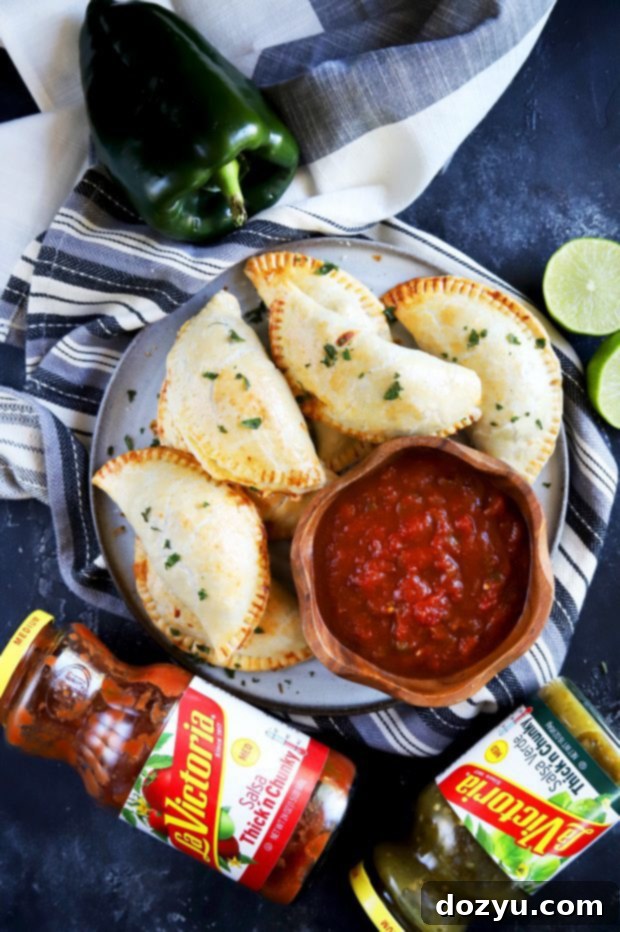 Poblano-Infused Chicken Enchilada Empanadas 5 An overhead shot of multiple golden empanadas arranged artfully on a serving board, with a small bowl of LA VICTORIA® salsa ready for dipping, highlighting the vibrant colors and textures.