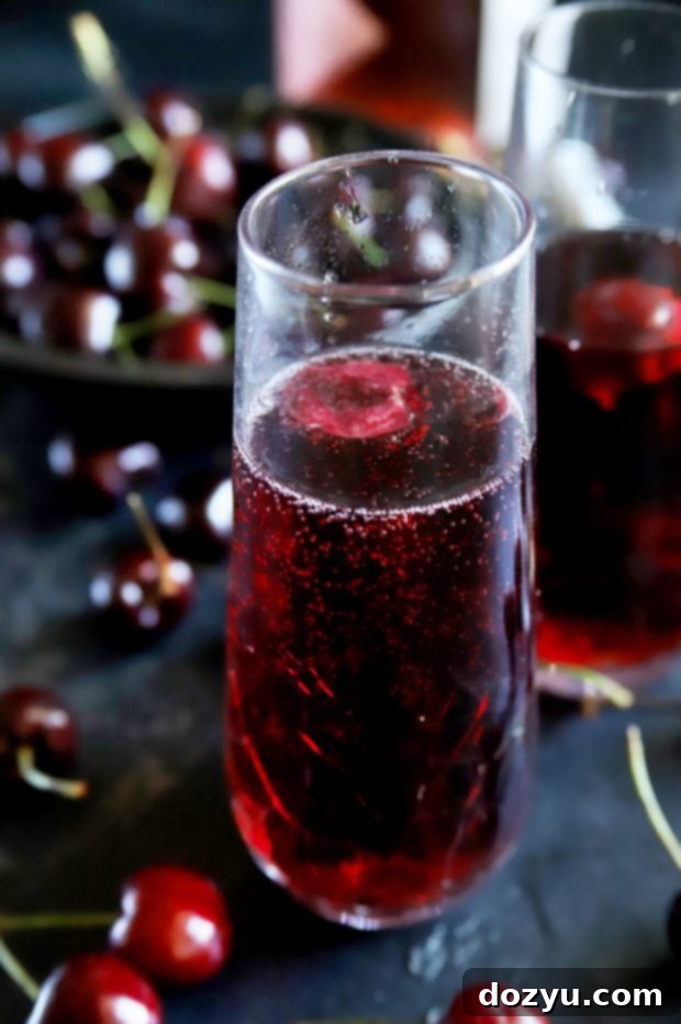 Close-up of a vibrant cherry red mimosa with a fresh cherry garnish and a hint of rosé