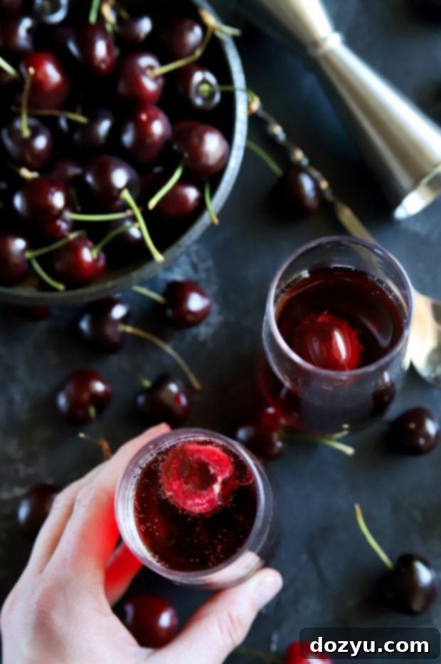 A hand reaching to pick up a champagne flute filled with a fresh cherry rosé mimosa, surrounded by loose cherries